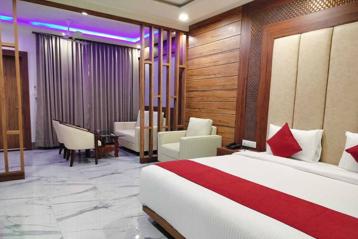 A hotel room with a large bed, two white armchairs, a wooden partition, and a marble floor.