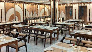 A spacious dining area with multiple tables and chairs, a chandelier, and a modern ceiling design. - Prime beach resort  Mandarmani (Kanthi)
