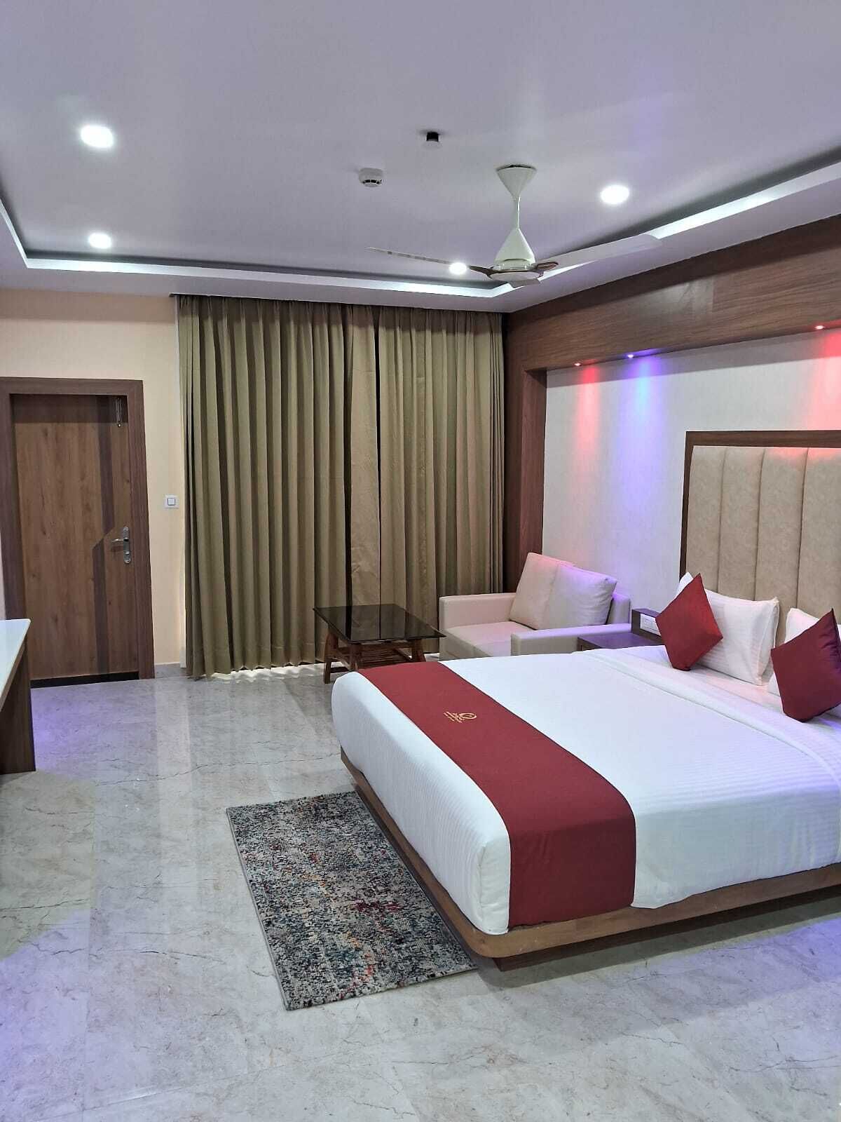 A hotel room with a large bed, a desk, a chair, a small table, and a ceiling fan.