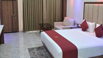 A hotel room with a large bed, a desk, a chair, a small table, and a ceiling fan.