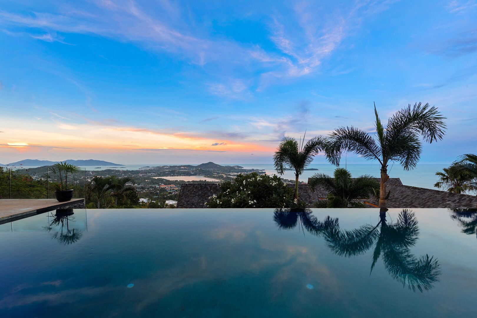 An infinity pool with a clear view of the ocean and distant mountains during sunset.