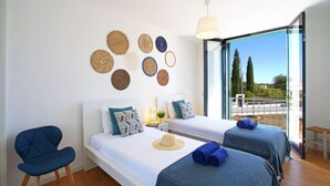 A modern hotel room with two beds, a blue chair, and a large window offering a view of the outdoors. - Precious time by Interhome (Tavira)