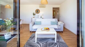 A modern living room with a white sofa, a white coffee table, and a large window. - Precious time by Interhome (Tavira)