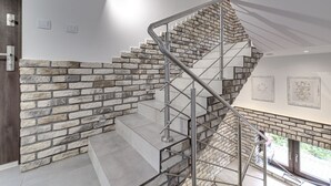 Un escalier moderne, avec un mur en pierre d’un côté et une rampe en métal de l’autre.