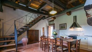 A spacious kitchen with a large dining table, wooden chairs, a built-in stove, and a rustic staircase. - Il Piccione by Interhome (Pitigliano)