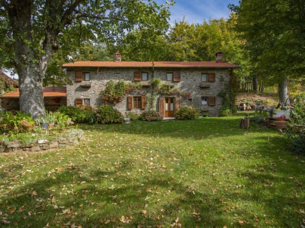 A stone house with a red roof, a front door, and a small front yard with grass and trees. - I 3 Faggi by Interhome (Pistoia)