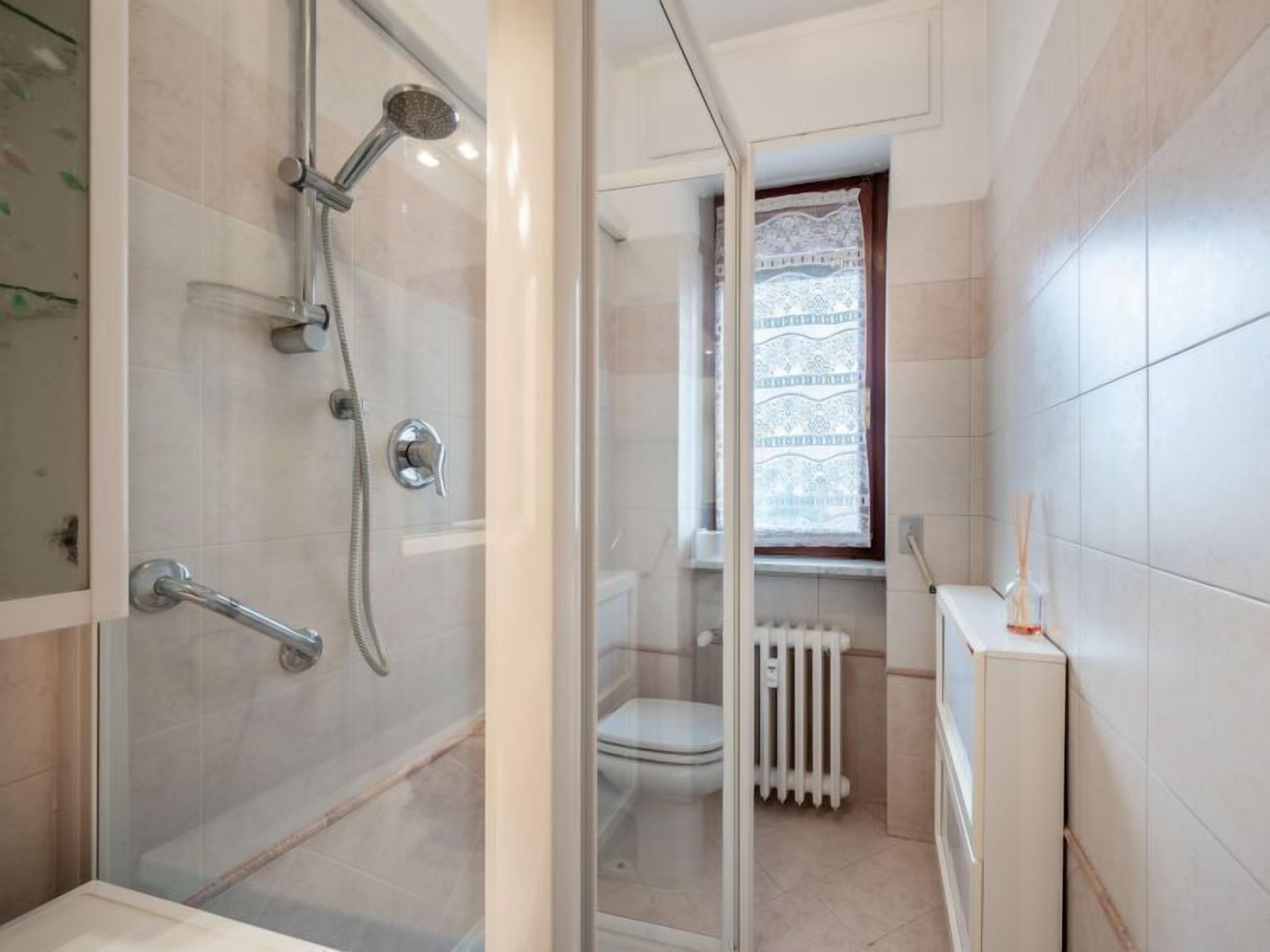 A modern bathroom with a glass-enclosed shower, a toilet, and a radiator.