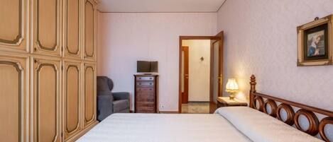 Ein Hotelzimmer mit großem Kleiderschrank, einem Bett, einem Schreibtisch mit Lampe sowie einem Fernseher.