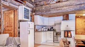 A log cabin interior with a kitchen area, including a refrigerator, microwave, stove, and cabinets.