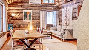 A cozy log cabin interior with a wooden dining table, chairs, a sofa, and a fireplace.
