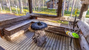 A wooden deck with a bench and a table, surrounded by a forest.
