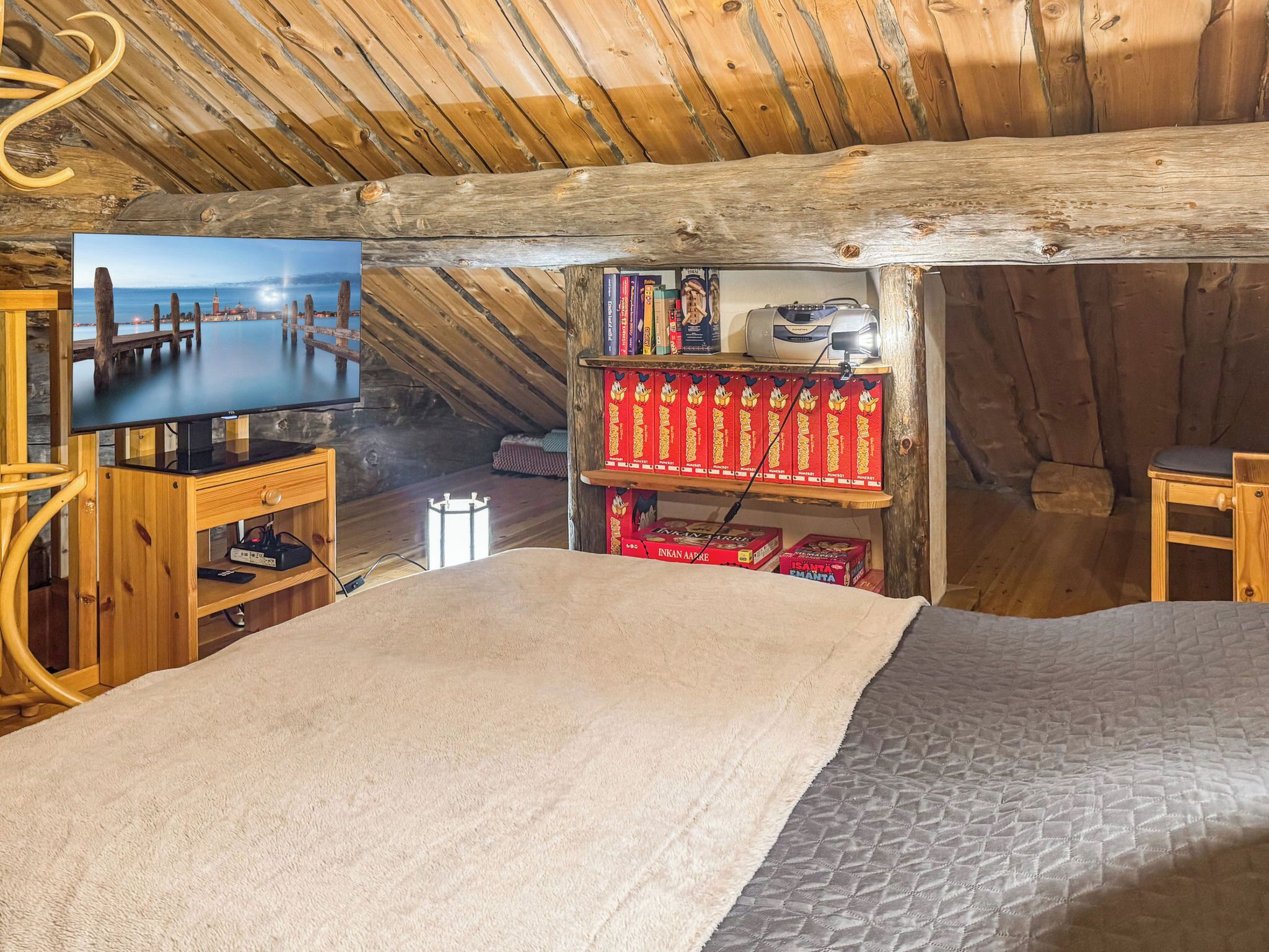Un dormitorio estilo ático acogedor con televisión, estanterías de madera y cama.