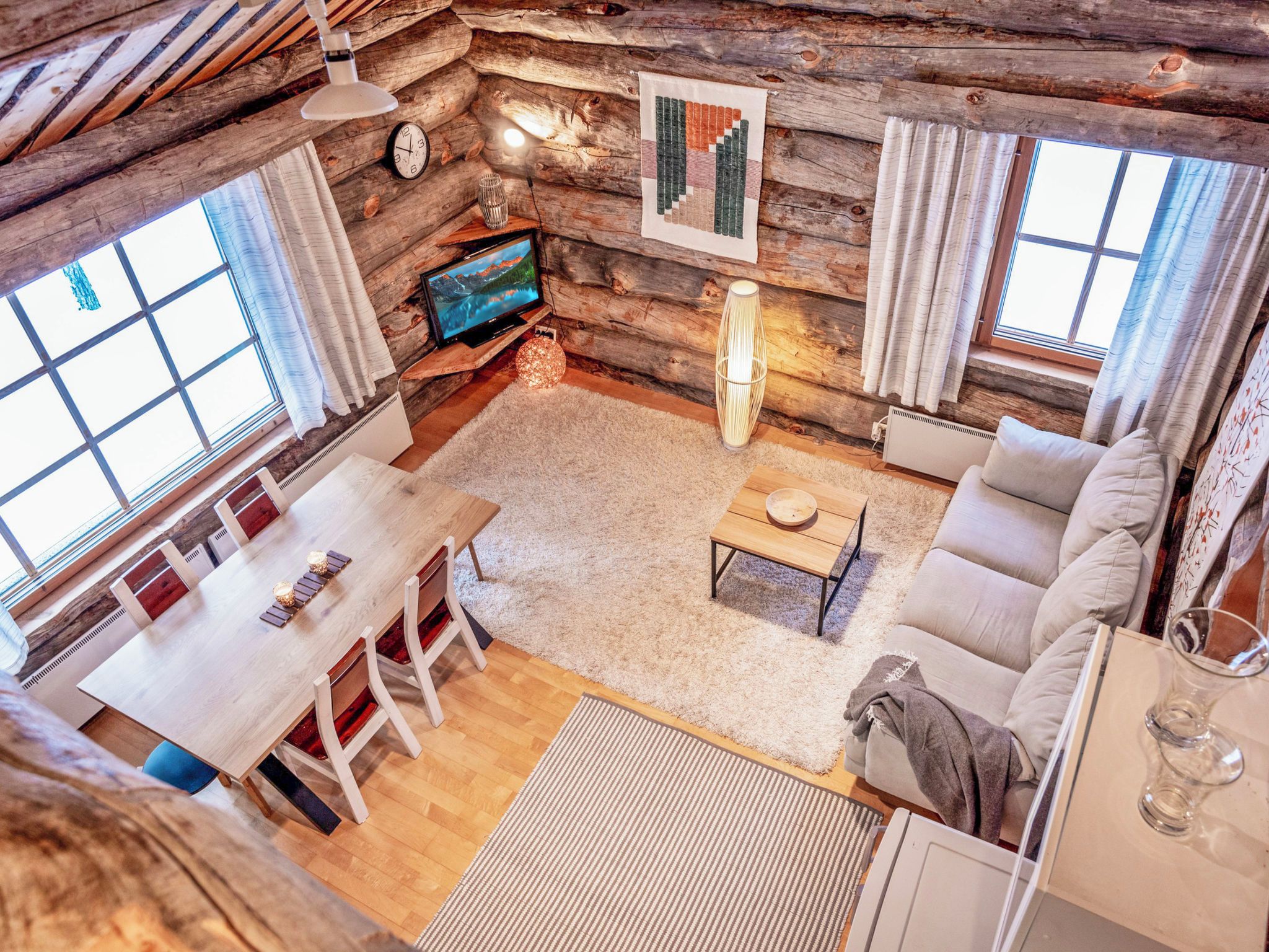 Interior acolhedor de uma cabana de madeira, com área de jantar, sofá e televisão.