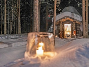 A cozy cabin with a lit candle in the foreground, surrounded by snow-covered ground and trees. - Rukanlumous 3 by Interhome (Kuusamo)