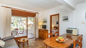 A cozy living area with a sofa, a dining table with chairs, a TV, and a kitchen area with a microwave. - "Melis II M4 Playa de Pals" by Interhome (Pals)