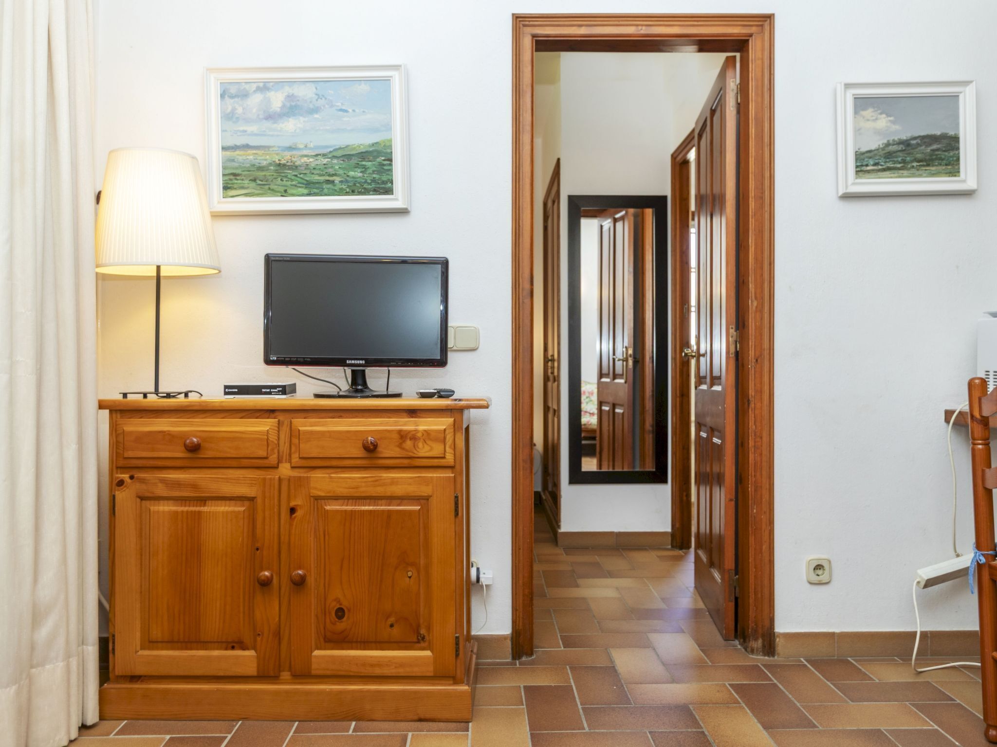 A hotel room with a wooden cabinet, a television, and two framed landscape paintings on the wall.