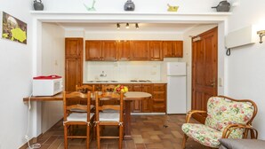 Une cuisine compacte avec des meubles en bois, une table à manger avec des chaises, un réfrigérateur et un fauteuil à motifs floraux.