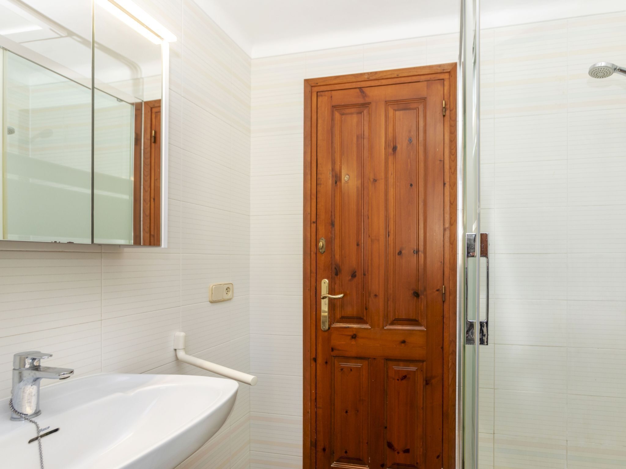 Een badkamer met een houten deur, een witte wastafel met een chroom kraan en een spiegel erboven.