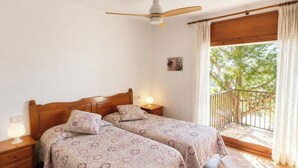 A bedroom with two beds, a ceiling fan, a nightstand with a lamp, a window with curtains, and a balcony with a railing. - "Melis II M8 Playa de Pals" by Interhome (Pals)