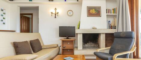 A living room with a sofa, armchair, and coffee table. There is a fireplace, a television, and a bookshelf.