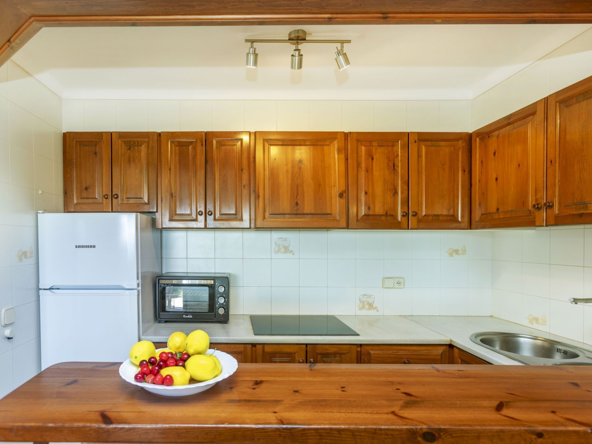 Una cocina con armarios de madera, un refrigerador Liebherr, un horno tostador y un cuenco de fruta en la encimera.