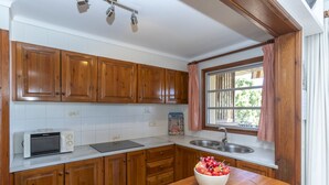 A kitchen with wooden cabinets, a microwave, a sink, and a window with curtains.