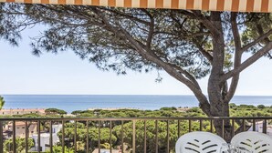A balcony with a table set for dining, overlooking a coastal view with a tree and buildings in the background.