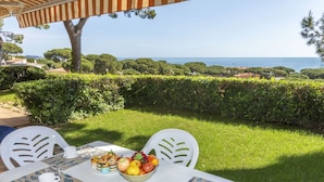 An outdoor dining area with a table set for four, surrounded by white chairs, a view of the sea, and a well-maintained garden.