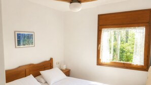 A bedroom with a wooden bed, a nightstand, a ceiling fan, a window with lace curtains, and a framed picture on the wall.