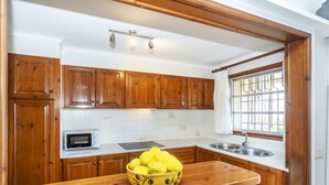 A kitchen with wooden cabinets, a microwave, a sink, and a window with bars.