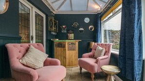 Una habitación acogedora con dos sillones rosados, una mesita redonda pequeña y una zona de bar con un letrero que dice "Bar".