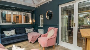 Una habitación acogedora con una pared azul oscuro, un sillón rosa, un sofá azul y una mesa blanca.