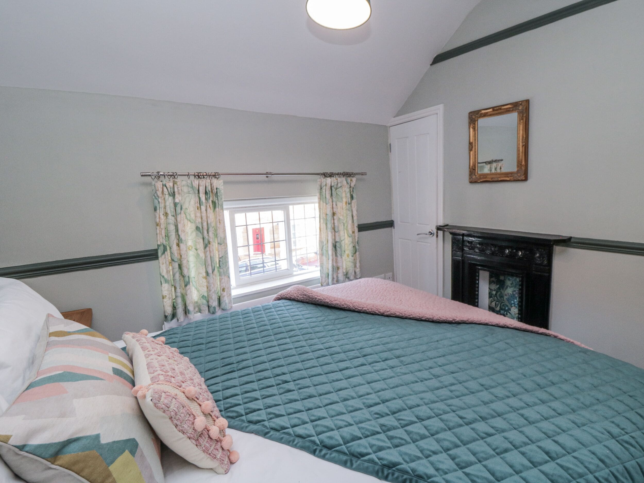 A bedroom with a bed, a window with curtains, a fireplace, and a mirror on the wall.