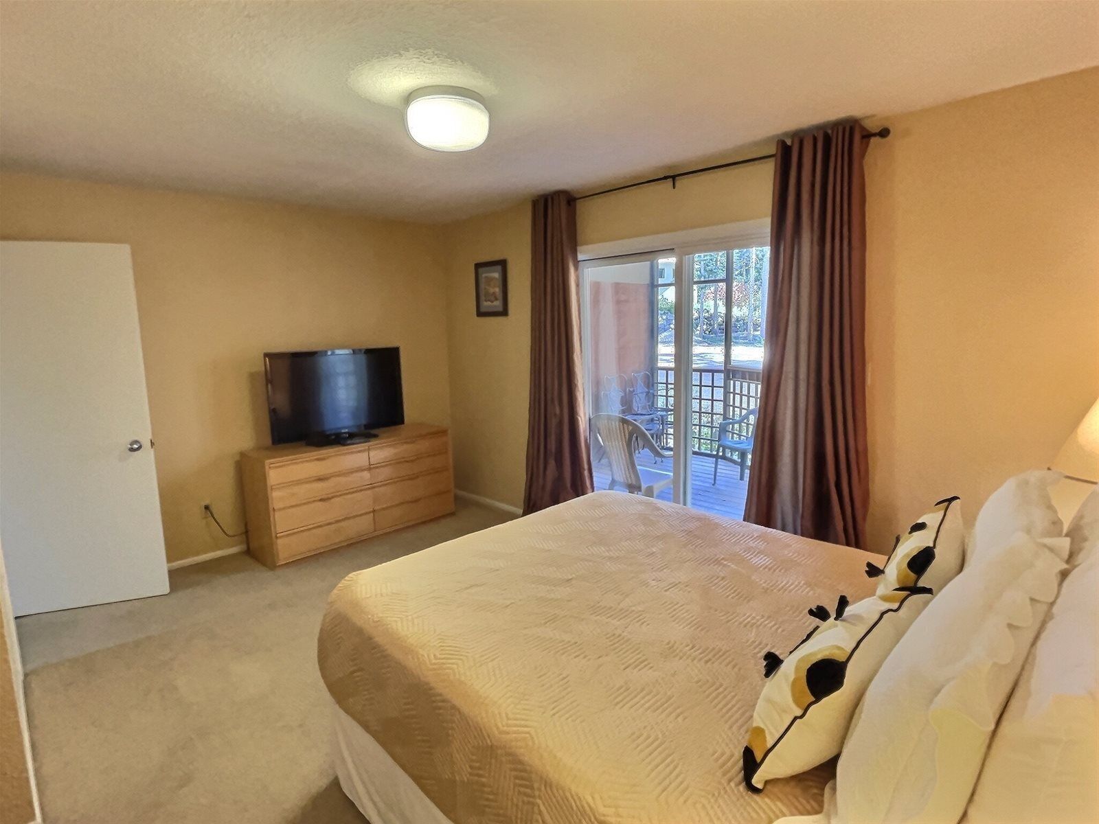 Una habitación de hotel con una cama, un televisor sobre un aparador de madera y un balcón con sillas.