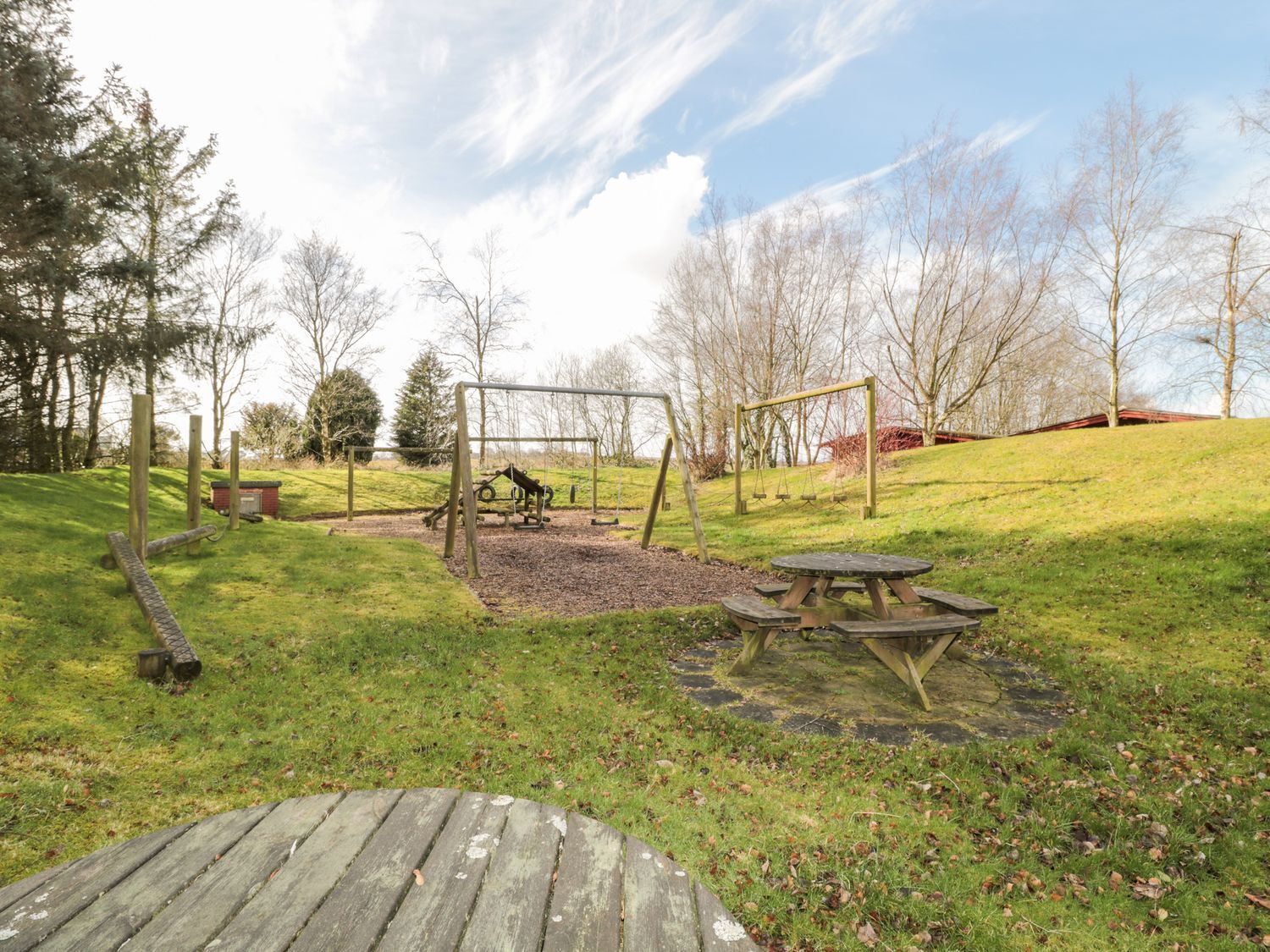 Un parque con un columpio, una mesa de picnic y un cobertizo pequeño.