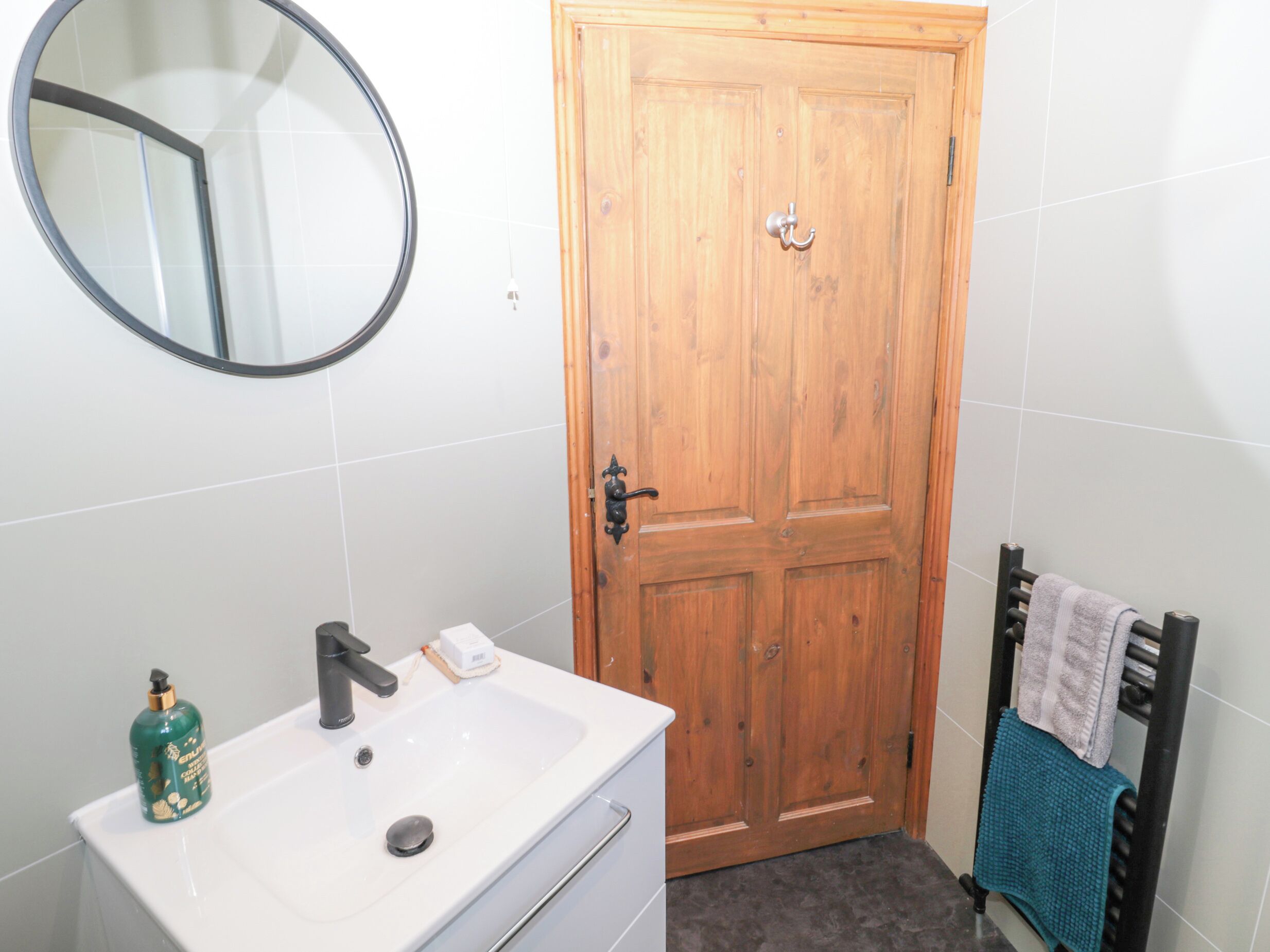 A bathroom with a white sink, a mirror, a wooden door, and a towel rack with towels.
