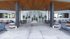 Un hall d’entrée spacieux avec un plafond haut, des espaces de détente modernes et une structure à colonnes centrale.