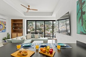 A modern living room with a sofa, dining table with breakfast, city view, and artwork. - 1BD 2Baths at Casa Madero 320 An Old Town Gem 1BD Condo for rent in Old Town, Pu (Puerto Vallarta)