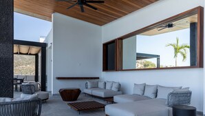 Un salon moderne doté d’une grande fenêtre, d’un ventilateur de plafond et d’un espace détente avec des canapés et une table basse.