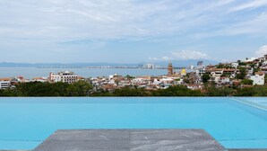 Une piscine offrant une vue sur un paysage urbain côtier, avec des bâtiments et une chaîne de montagnes lointaine.