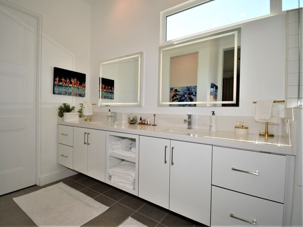 Une salle de bain moderne avec des meubles blancs, un grand miroir et un sol carrelé.