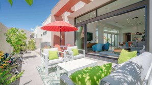 An outdoor patio area with white furniture, a red umbrella, and a glass door leading to an interior living space. - P S Chic Escape (Palm Springs)