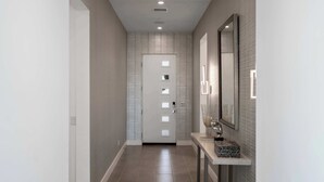 A hallway with a door, a console table with a sculpture, and a mirror with lights. - P S Chic Escape (Palm Springs)