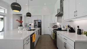 Une cuisine moderne avec des meubles blancs, des appareils en acier inoxydable et des luminaires suspendus.