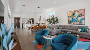 A modern living room with a sofa, two armchairs, a coffee table, and a dining area with a kitchen in the background. - P S Chic Escape (Palm Springs)