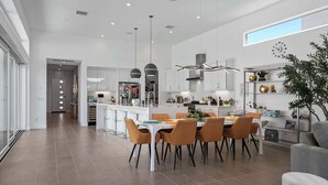 A modern kitchen with white cabinets, a central island, and a dining area with orange chairs. - P S Chic Escape (Palm Springs)