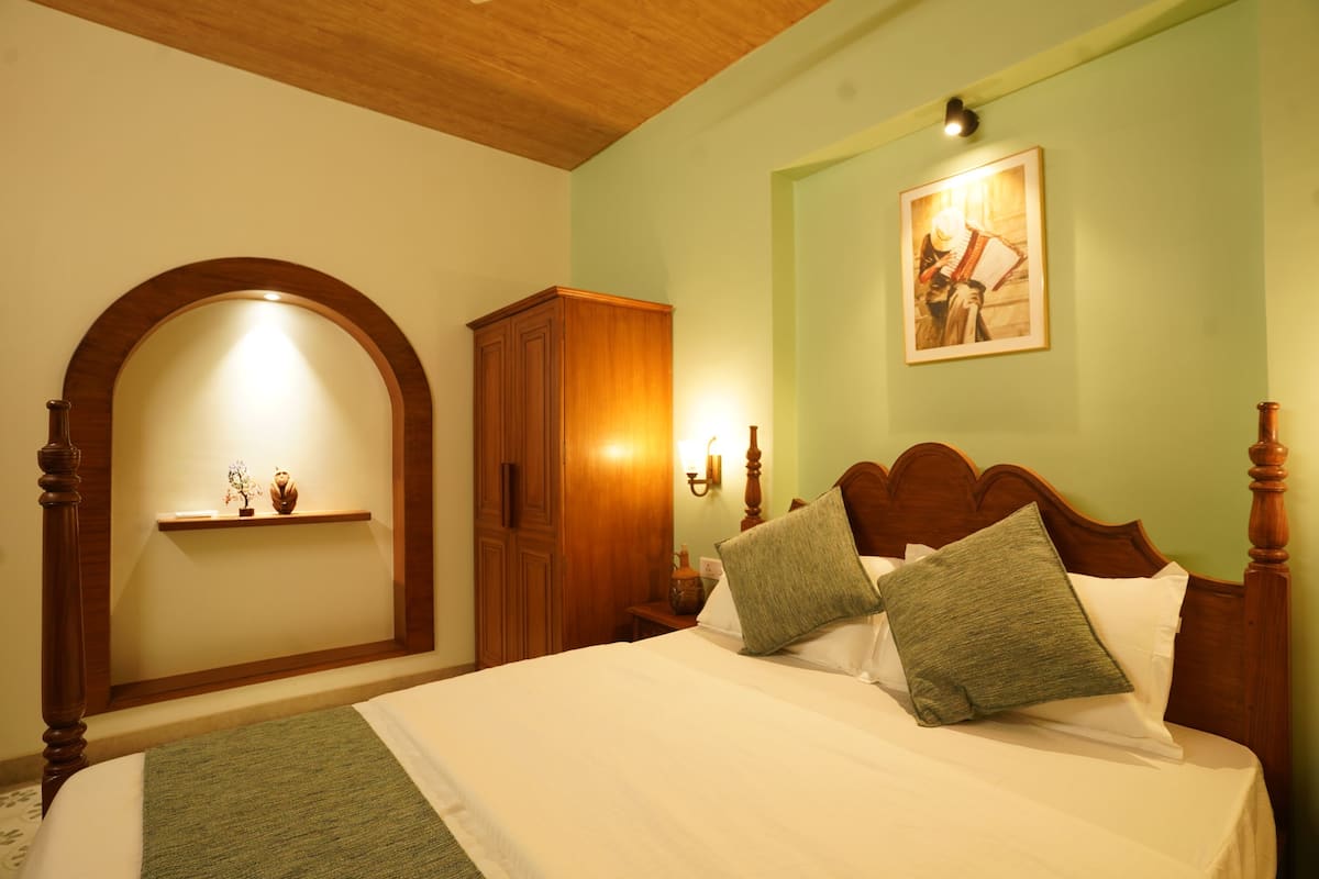 A bedroom with a large bed, wooden headboard, and a nightstand with a lamp.
