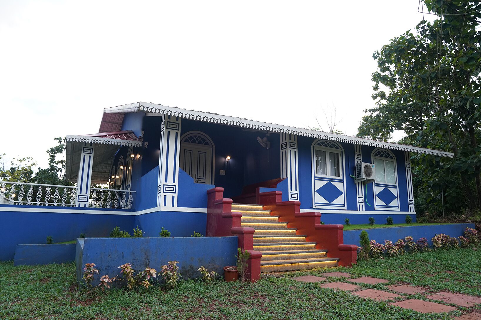 Un edificio de dos pisos con fachada azul, escalera roja y barandilla de balcón blanca.