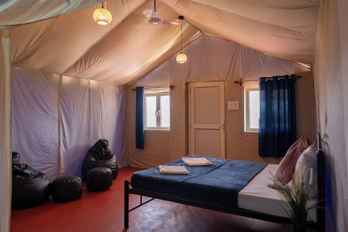 A tented room with a bed, two bean bags, a window, and a door.