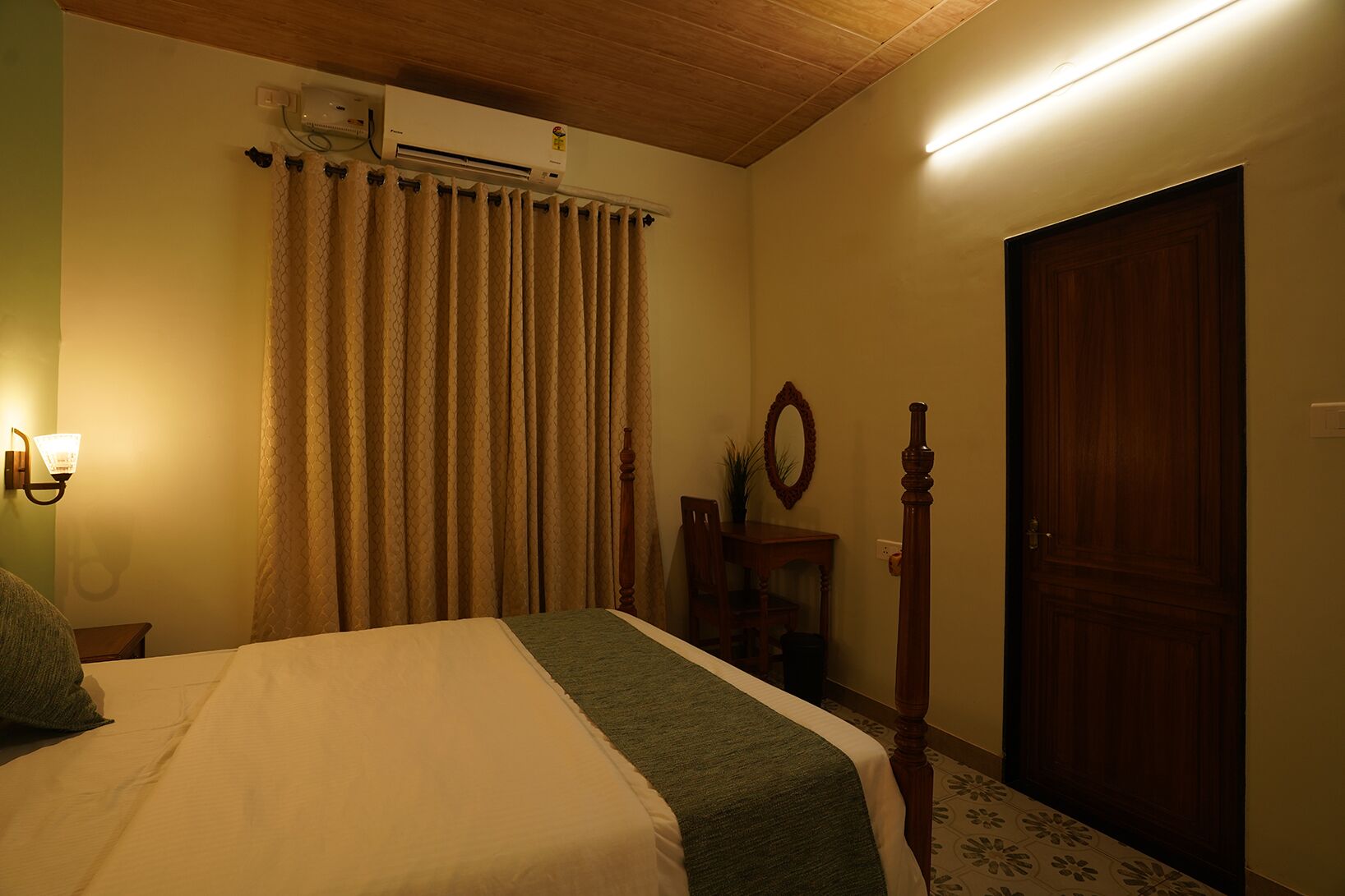 Een slaapkamer met een bed, een airconditioner, een houten deur en een spiegel aan de muur.